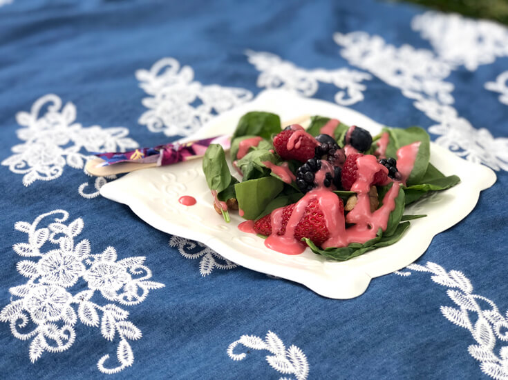 Plate of spinach salad with raspberry poppyseed dressing on blanket for a charming summer picnic party